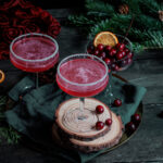 Der Cocktail Ginopolitan in zwei Cocktailgläsern, vor einem Hintergrund in Weihnachtsoptik